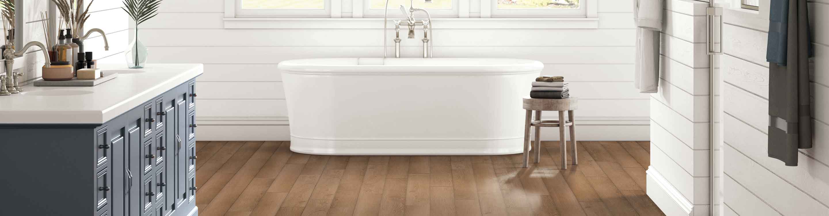 wood look vinyl flooring in modern bathroom with shiplap walls, blue vanity and white soak tub